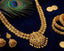 Gold necklace, earrings, and bangles on a dark blue fabric background with peacock feathers.