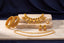 A gold jewelry set displayed on a marble slab against a dark blue fabric backdrop. The set includes a necklace, matching earrings, a bracelet, and a chain, decorated with gold, white pearls, and red stone accents.