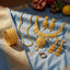 a gold set of bangles, necklace, chain, Jhumka earrings, and wedding band ring arranged on a baby blue sari with an assortment of summer fruits in the background